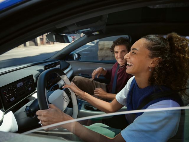 Eine Frau sitzt lachend auf dem Fahrersitz eines blauen VW ID. Polo Style, auf dem Beifahrersitz sitzt ein Mann.