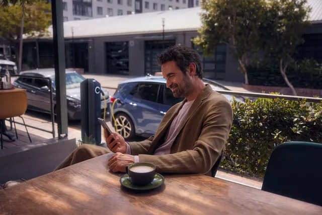 Ein Mann sitzt im Café und checkt per Smartphone den Ladestatus seines VW ID.3 Neo
